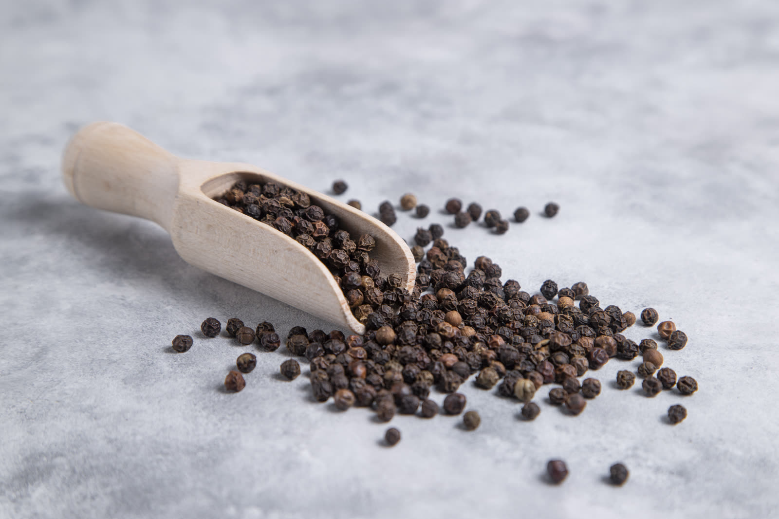 A wooden spoon full of black pepper corns placed on stone table